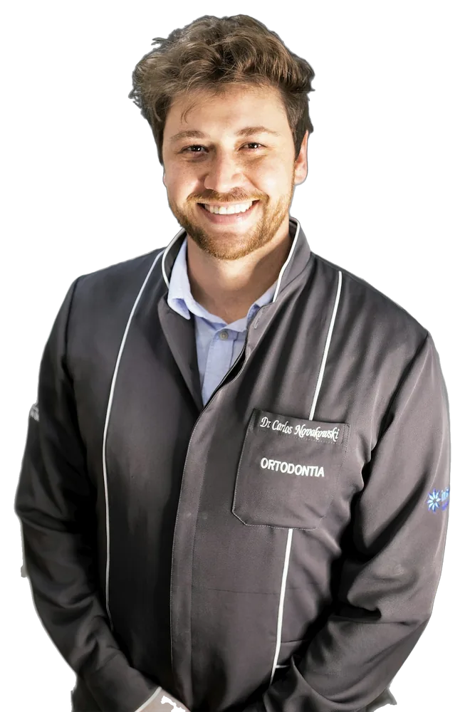 Dentista sorrindo, de jaleco escuro, no consultório